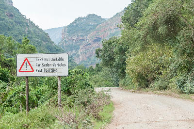 Warning sign on the R332 at the eastern entrance to the Baviaanskloof Wilderness Area, with rugged cliffs and gravel road scenery in the Eastern Cape, South Africa.