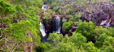 Elevated view of the twin waterfalls at Florence Falls flowing into a dark plunge pool, with upstream cascades, rocky cliffs and dense green woodland in Litchfield National Park, Northern Territory, Australia.
