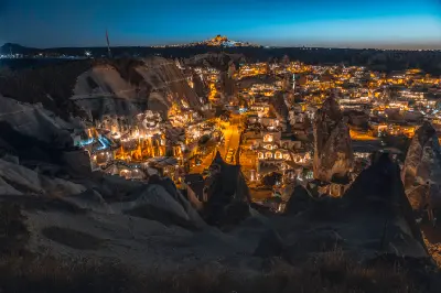 Night view of Göreme Town in Cappadocia featuring illuminated cave hotels, fairy chimneys and Uçhisar Castle on the horizon.