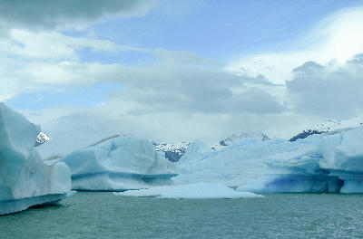 Floating blue icebergs on Lago Argentino with mountains in the background in Patagonia, Argentina.