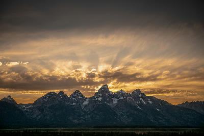 Sunbeams radiating behind the Grand Teton Range with silhouetted peaks at sunset in Wyoming.