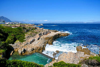 Rocky granite coastline and tidal pool along the Hermanus Cliff Path with waves breaking into Walker Bay, Western Cape, South Africa.