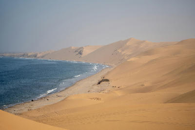 Wide coastal view of large sand dunes meeting the Atlantic Ocean along the Skeleton Coast in Namibia.