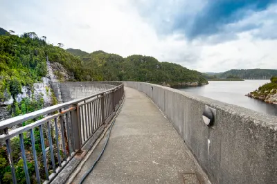 Walkway across the curved crest of Gordon Dam overlooking Lake Gordon and forested mountains in southwest Tasmania, Australia.