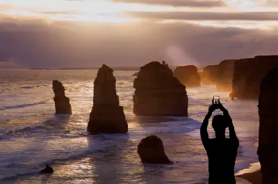 Photographer capturing the Twelve Apostles sea stacks at sunset on the Great Ocean Road, Victoria.
