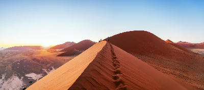 Sunrise view from Dune 45 in Sossusvlei, Namibia, with hikers and footprints along the red sand dune ridge.
