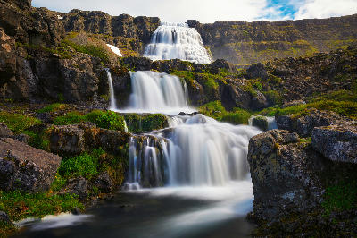 Dynjandi waterfall in the Westfjords region of northwestern Iceland, with broad multi-level cascades flowing down rocky slopes in a long-exposure scene.