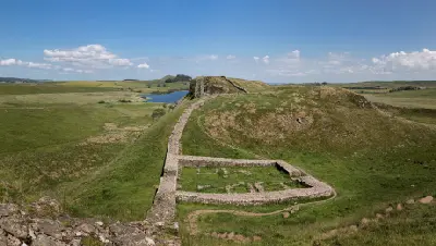Elevated view of Milecastle 39 ruins and Hadrian's Wall crossing Highshield Crags, with Crag Lough and rolling Northumberland countryside in the background.