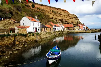 Blue-and-white fishing boat moored in Staithes Beck, with traditional waterfront cottages, colourful bunting and sandstone cliffs in North Yorkshire, England.