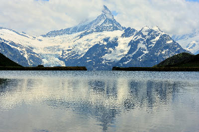 Snow-covered alpine peak reflected in Bachalpsee with still water and grassy lake edges near Grindelwald, Bernese Alps, Switzerland.