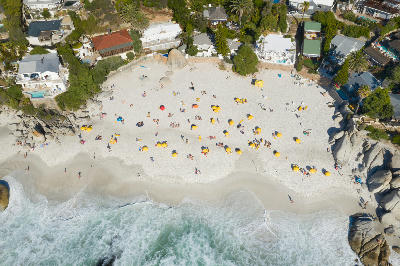 Top-down aerial of Clifton Third Beach showing a compact white sand cove with umbrellas, granite boulders, and houses above the shoreline.