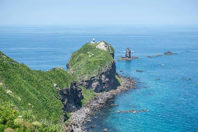 Cape Kamui headland with lighthouse and coastal cliffs above clear blue water in Hokkaido, Japan.