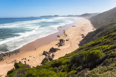 Elevated view of Diaz Beach near Mossel Bay with rolling surf, rocky outcrops, coastal dunes and a long sandy shoreline extending into the distance.