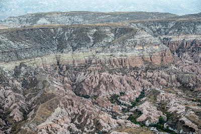 Aerial view of Red Valley in Cappadocia, Turkey, with layered volcanic cliffs, winding trails and deeply eroded pink and cream rock formations.