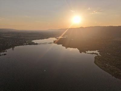 Aerial view of Hartbeespoort Dam at sunset with calm water, a bridge crossing the lake and the Magaliesberg mountain range on the horizon.