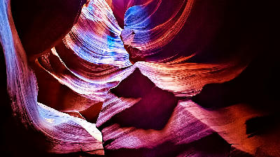 Looking up inside Upper Antelope Canyon in Arizona, showing smooth curved sandstone walls with vibrant pink and purple light reflections and abstract rock patterns.