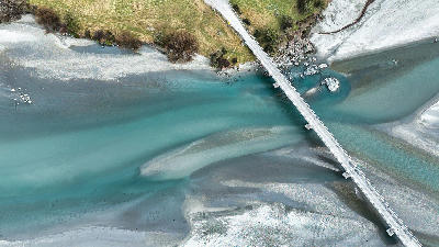 Aerial view of turquoise channels of the braided Dart River flowing beneath a road bridge near Glenorchy, South Island, New Zealand.