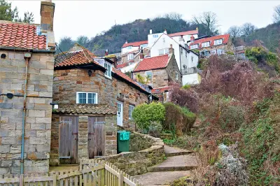 Traditional stone cottages with red-tiled roofs cluster along a narrow hillside footpath in Runswick Bay, a historic coastal village in North Yorkshire, England.