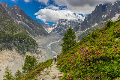Hikers walking along a mountain trail overlooking the Mer de Glace glacier and alpine valley in the French Alps near Chamonix.