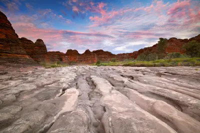 Eroded channels in the dry bed of Piccaninny Creek lead toward striped sandstone domes beneath a pink sunrise sky.