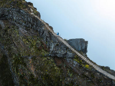 Hiker ascending a steep stone staircase carved into a volcanic ridge on the Pico do Arieiro–Pico Ruivo trail in Madeira.
