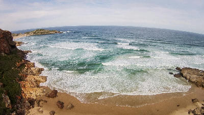 View of Robberg Peninsula extending into the ocean with waves breaking onto a sandy beach near Plettenberg Bay, South Africa.