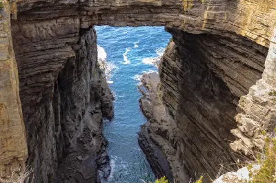 Ocean channel beneath Tasman Arch between steep layered rock walls on the Tasman Peninsula, Tasmania.