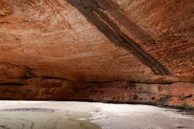 Towering red sandstone walls curve around the sandy floor and shallow water of Cathedral Gorge in Purnululu National Park.