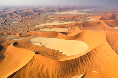 High aerial view of massive orange Namib dunes surrounding the pale clay pans of Deadvlei in Namibia.
