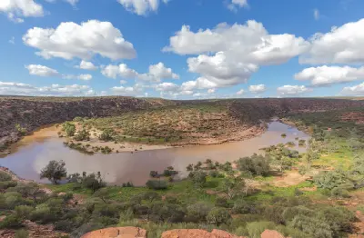 Wide elevated view of the Murchison River bending around a rocky ridge, with green vegetation and steep gorge walls beneath a blue sky.