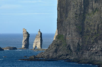 Person lying near the edge of Eiðiskollur cliff overlooking the Risin og Kellingin sea stacks in the Atlantic Ocean, Faroe Islands.