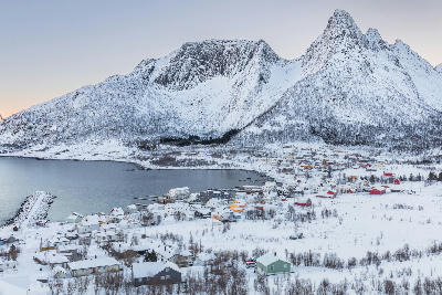 Winter view of Senjahopen village with houses along the fjord and steep snow-covered mountains behind, Senja island Norway