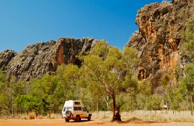 Four-wheel-drive vehicle parked beneath rugged limestone cliffs and eucalyptus trees near the entrance to Tunnel Creek.