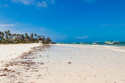 White sandy shoreline with traditional fishing boats, turquoise Indian Ocean and beachfront lodges at Matemwe Beach, Zanzibar, Tanzania.