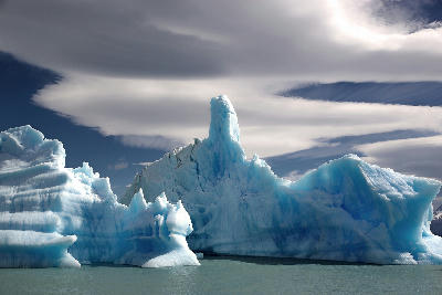 Large blue iceberg formations floating on Lago Argentino under dramatic clouds in Patagonia, Argentina.