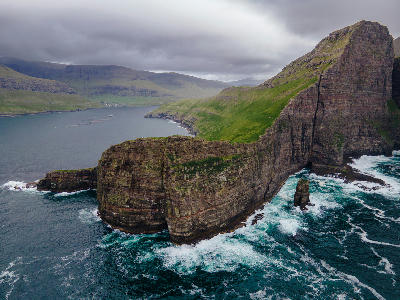 Aerial view of Drangarnir sea arch and steep coastal cliffs with Tindhólmur visible offshore on Vágar Island, Faroe Islands.