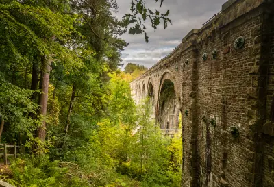 Close side view of Lambley Viaduct's tall stone arches extending through dense green woodland above the River South Tyne valley in Northumberland.
