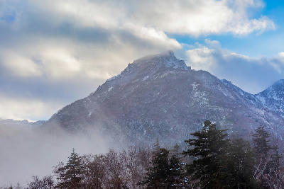 Mount Kurodake partially covered in snow with clouds and mist drifting across the peak in Daisetsuzan National Park, Hokkaido, Japan.