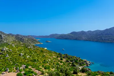 Rocky green hillside with ancient Lycian sarcophagi overlooking deep blue Mediterranean waters in the Kekova region of Antalya, Turkey.