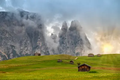 Alpine huts on rolling green meadows of Alpe di Siusi with the Schlern mountains rising behind in the Dolomites, South Tyrol, Italy.