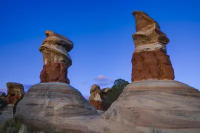Towering red and cream sandstone hoodoos rise against a deep blue evening sky in Devil’s Garden.