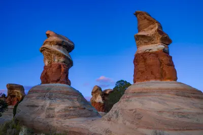 Towering red and cream sandstone hoodoos rise against a deep blue evening sky in Devil’s Garden.