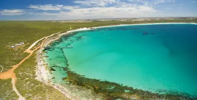 Aerial panorama of Vivonne Bay on Kangaroo Island, showing turquoise water, dark reef patterns, a long white beach and wooden jetty.