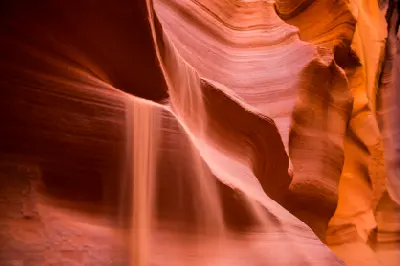 Falling sand cascading down smooth red sandstone walls inside Canyon X near Page Arizona in a narrow slot canyon formation.