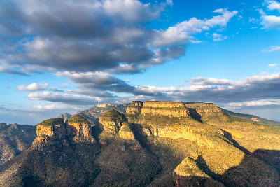 Golden light illuminating the Three Rondavels rock formations above Blyde River Canyon in Mpumalanga, South Africa, beneath dramatic cloud-filled skies.