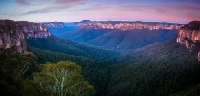 Panoramic twilight view from Govetts Leap across the forested Grose Valley, surrounded by towering sandstone escarpments beneath a pink and purple sky.