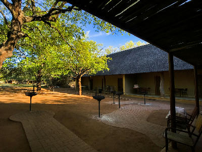 Shaded accommodation courtyard with thatched-roof chalets and braai facilities at Lower Sabie Rest Camp.