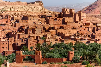 Dense mud-brick kasbah architecture of Aït Benhaddou in Morocco with oasis palms and fortified walls in the foreground.