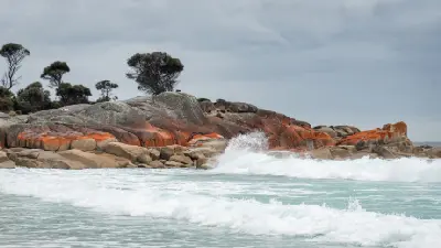 Waves breaking against orange lichen-covered granite rocks at Binalong Bay, Bay of Fires, Tasmania.