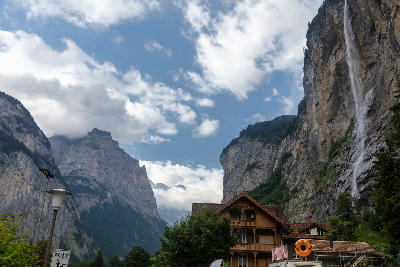 Staubbach Falls flowing down a cliff above houses in Lauterbrunnen Valley with mountains and clouds in Switzerland